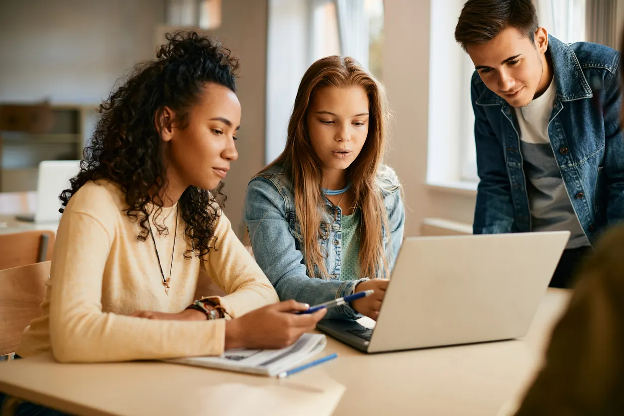Grupo de estudantes de inglês interagindo e colaborando em frente a um laptop, representando o aprendizado em grupo.