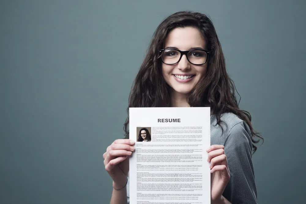 Mulher segurando currículo em inglês sorrindo para a câmera