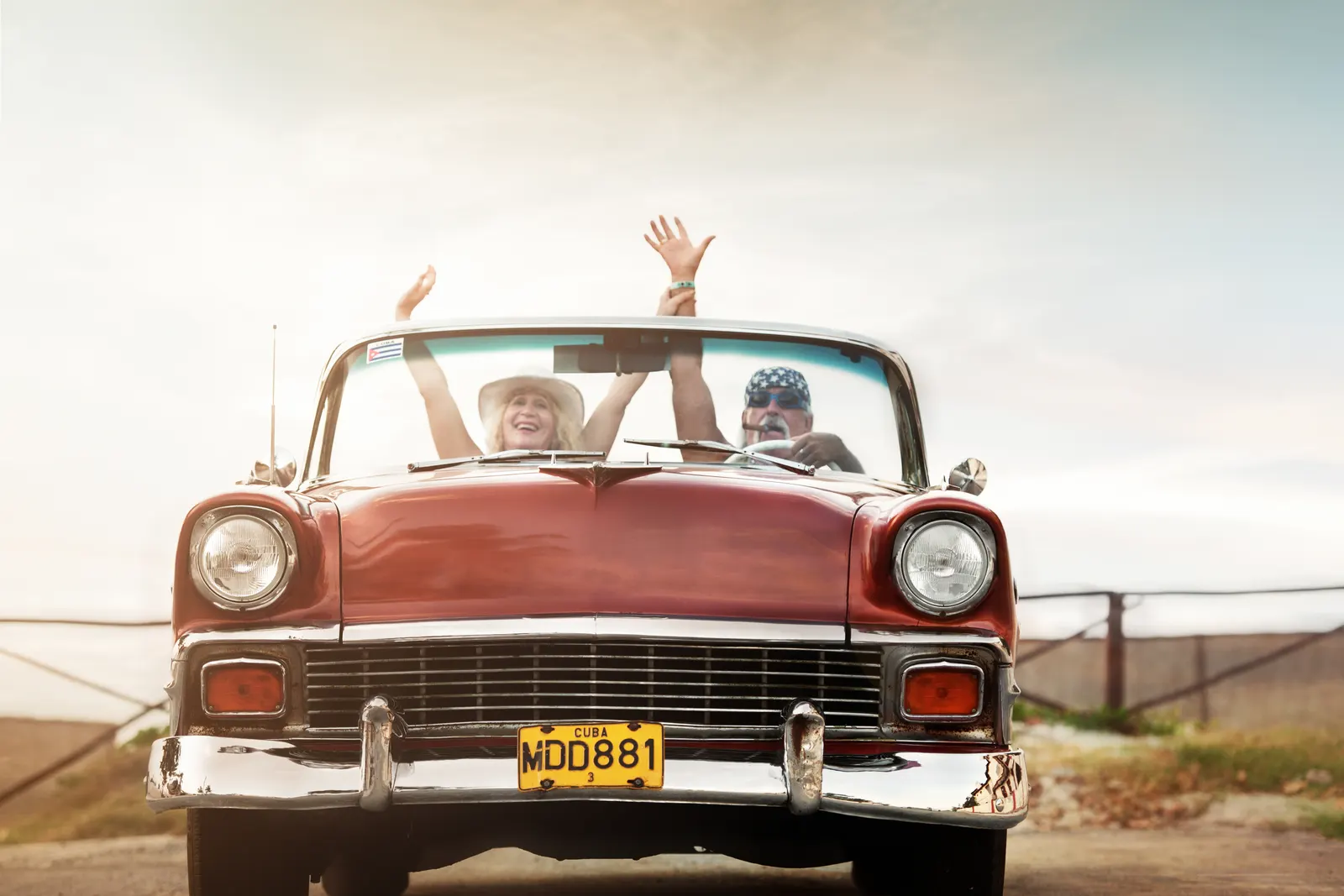 Duas pessoas sorrindo e comemorando dentro de um carro antigo conversível, ilustrando o sentimento de orgulho e carinho, como o 'xodó' por um objeto especial.