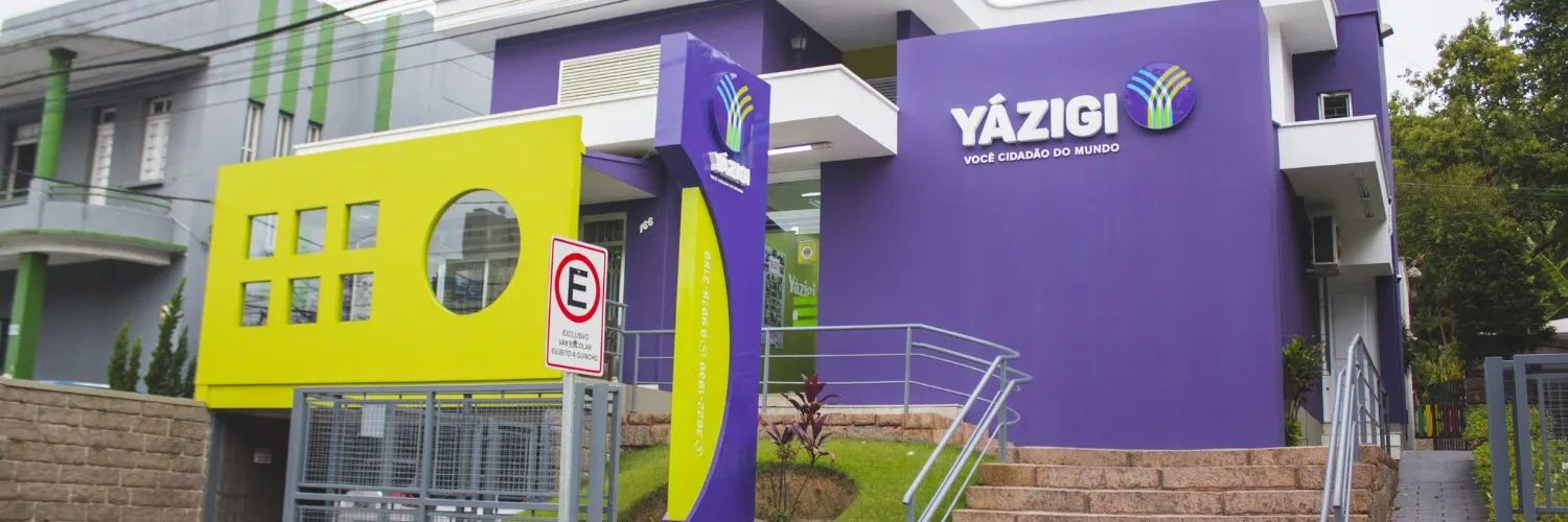 Imagem da fachada de uma unidade do Yázigi com as cores: roxo e verde e em uma das paredes o nome com a logo do Yázigi.