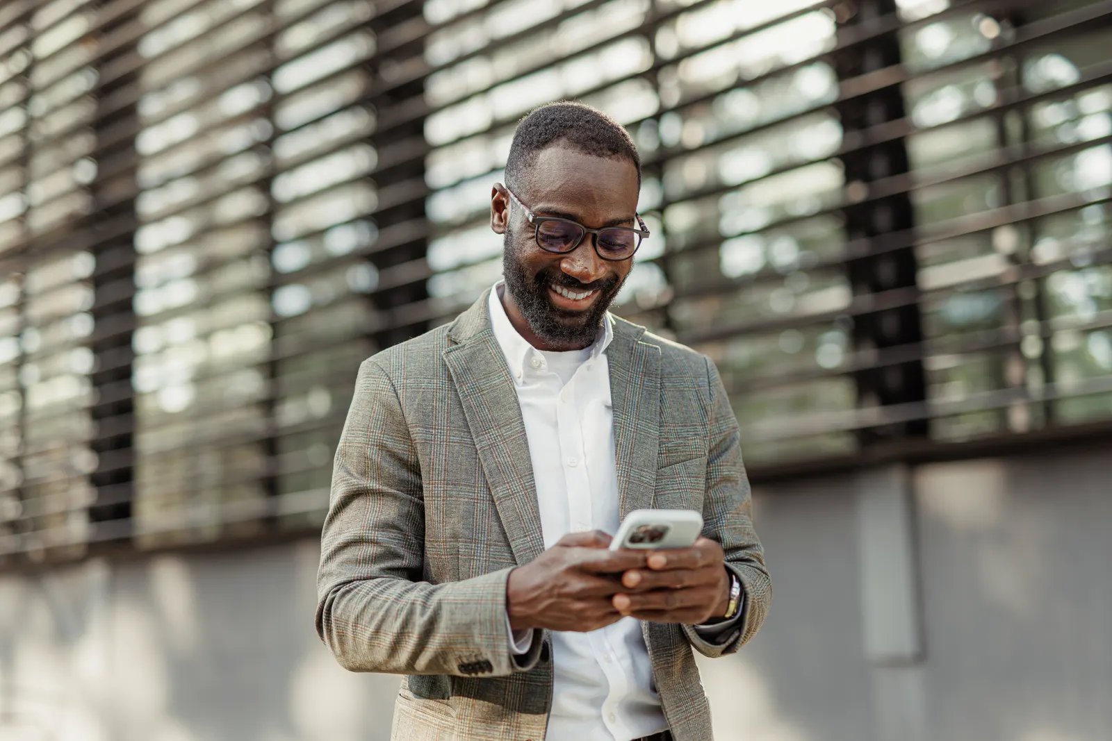 Imagem de um homem de terno e óculos, sorrindo enquanto olha pra baixo em direção ao seu celular. Ele usa as redes sociais em inglês.