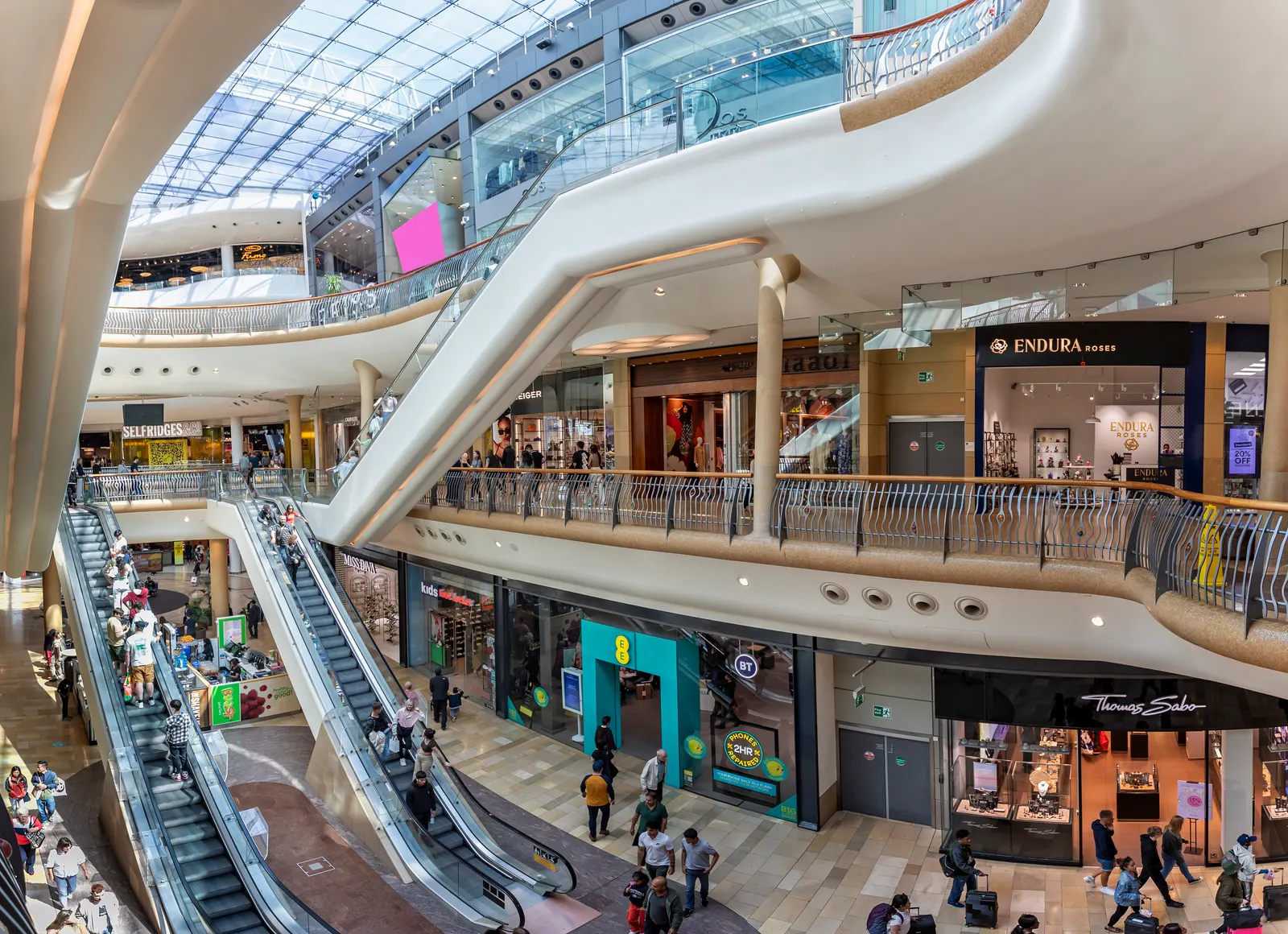 Imagem interna de um shopping. Podemos ver as escadas rolantes e a divisão de andares do shopping, que possui 3 andares com diversas lojas em cada um deles. A imagem serve para representar o termo de estrangeirismo 'Shopping'.