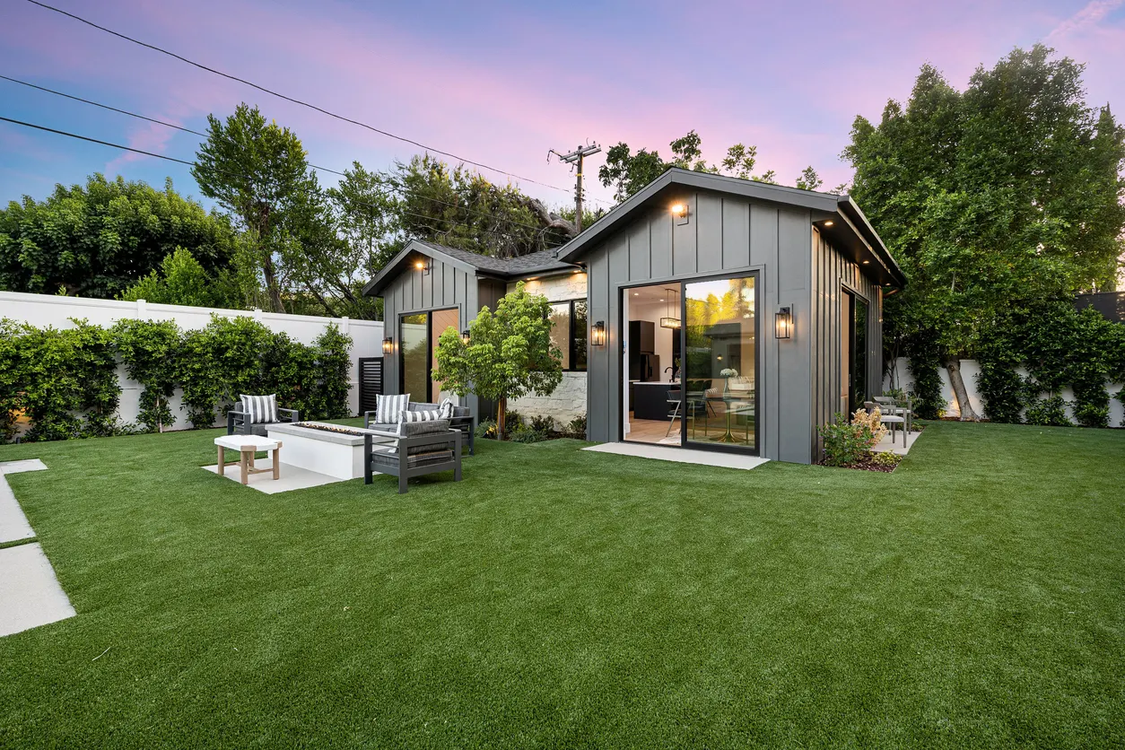 Casa moderna com fachada cinza e jardim bem cuidado ao pôr do sol.