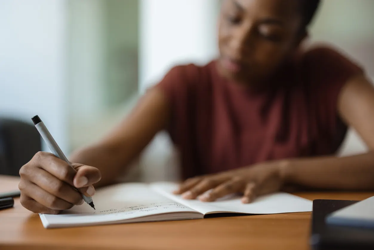 Mulher escrevendo em um caderno, simbolizando o estudo e a dedicação ao aprendizado de inglês.